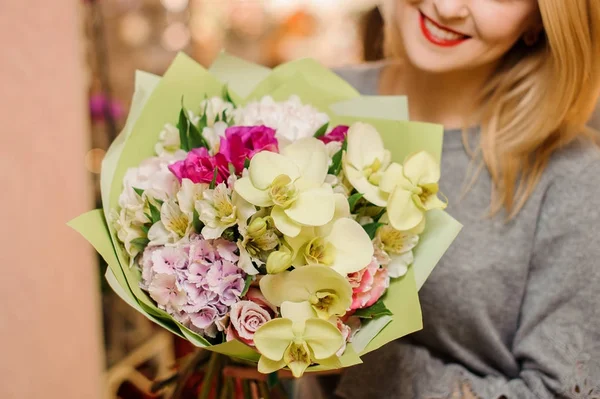 Fêmea loira sorri e segura um buquê com orquídeas, rosas e hortênsias — Fotografia de Stock