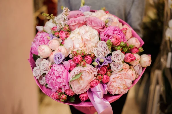 Дівчина тримає величезний букет з різних рожевих і фіолетових квітів — стокове фото