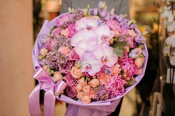 Fille tient un bouquet de différentes fleurs roses et violettes, y compris les orchidées — Photo
