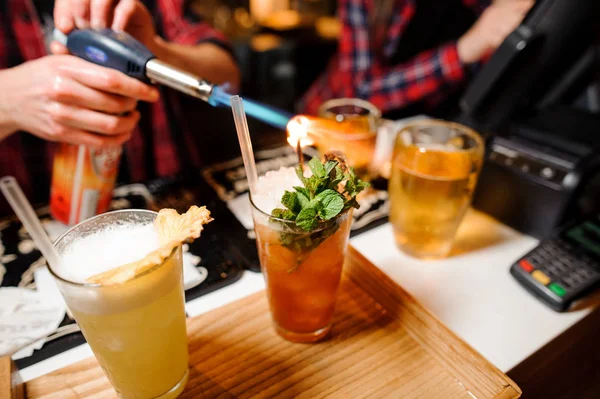 Barman sets fire to sprig of mint on orange-colored cocktails — Stock Photo, Image