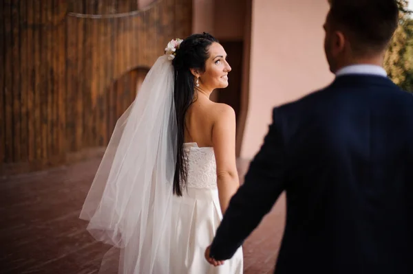 Brilho em um terno azul seguindo sua bela noiva sorridente vestida com um vestido branco — Fotografia de Stock