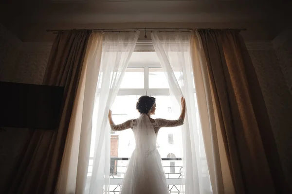 美丽的新娘穿着白色婚纱打开窗帘 — 图库照片