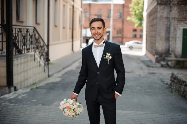 Bräutigam im schwarzen Anzug mit rosa Blumenstrauß auf der Straße — Stockfoto