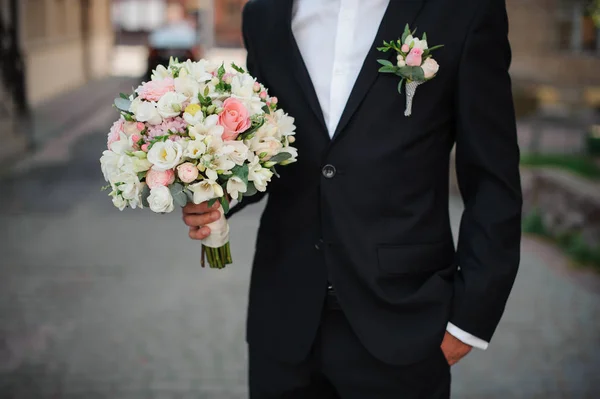 Noivo em um terno preto segurando um buquê de casamento suave — Fotografia de Stock