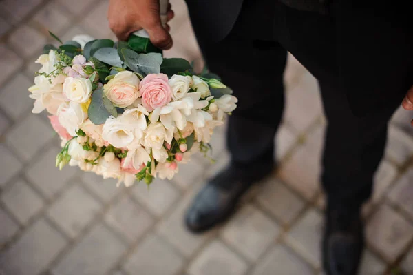 Noivo em um terno preto e sapatos clássicos segurando um buquê de casamento — Fotografia de Stock