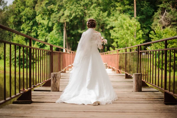 Noiva em um vestido de renda branco longo andando em uma ponte de madeira — Fotografia de Stock