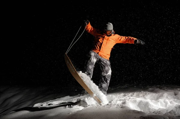 Snowboarder masculino em sportswear laranja balanceamento na neve à noite — Fotografia de Stock