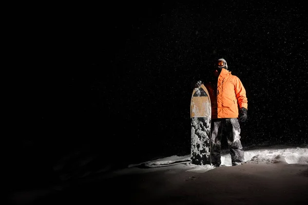 Erkek snowboard kar üzerinde kurulu ile portakal spor giyim ayakta geceleri — Stok fotoğraf