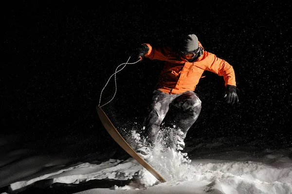 Profi-Snowboarder in orangefarbener Sportbekleidung springt nachts auf Schnee — Stockfoto
