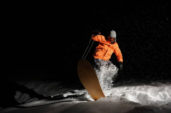 Snowboarder in orangefarbener Sportbekleidung balanciert nachts auf dem Snowboard — Stockfoto