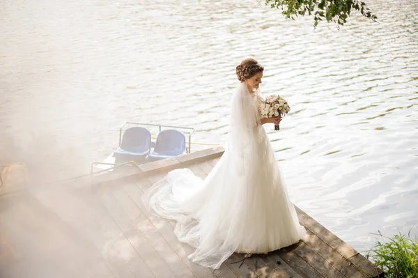 Piękna panna młoda w sukni ślubnej biały stojący w pobliżu rzeki — Zdjęcie stockowe