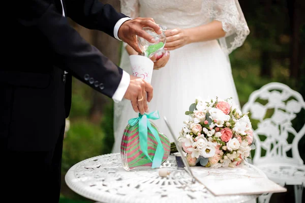 Bruidegom met bruid gieten multi gekleurd zand tegen de groene achtergrond — Stockfoto