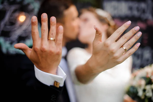 Noivo e noiva beijando e mostrando anéis de casamento em seus dedos — Fotografia de Stock