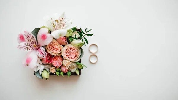 Dva zlaté snubní prsteny zařízený poblíž krásné a roztomilé květinová kompozice v krabici — Stock fotografie