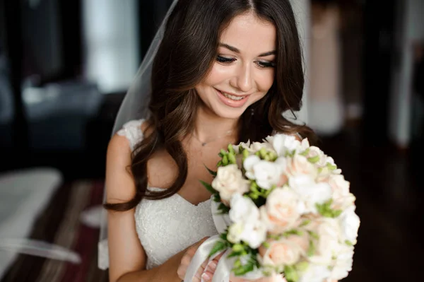 Preparación de la novia mañana. Hermosa y sonriente novia en un velo blanco con un ramo de bodas — Foto de Stock