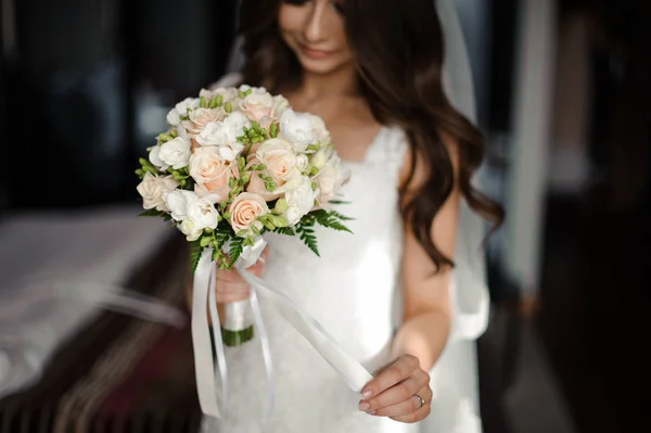 Preparación de la novia mañana. Hermosa novia vestida con un vestido blanco y un velo con un ramo de bodas — Foto de Stock