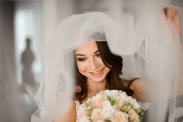 Bride morning preparation. Attractive and smiling bride in a white veil with a wedding bouquet