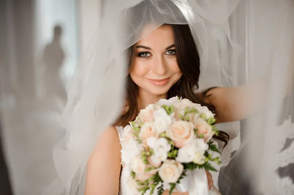 Preparación de la novia mañana. Novia feliz y sonriente en un velo blanco con un ramo de bodas — Foto de Stock