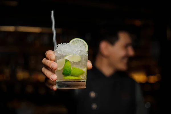 Bartender hand holding a glass filled with Caipirinha cocktail with a straw. Close up — Stock Photo, Image