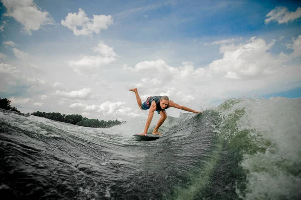 Joven y atlético hombre wakesurfing en el tablero por el río a —  Fotos de Stock