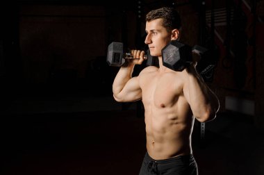Genç ve seksi adam crossfit iki ağır dambıl kullanarak bir spor salonunda pratik