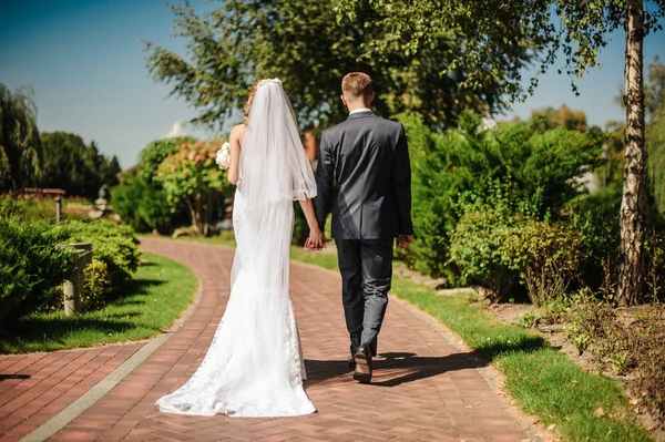 Noivo e em um vestido branco, com um buquê andam de mãos dadas — Fotografia de Stock