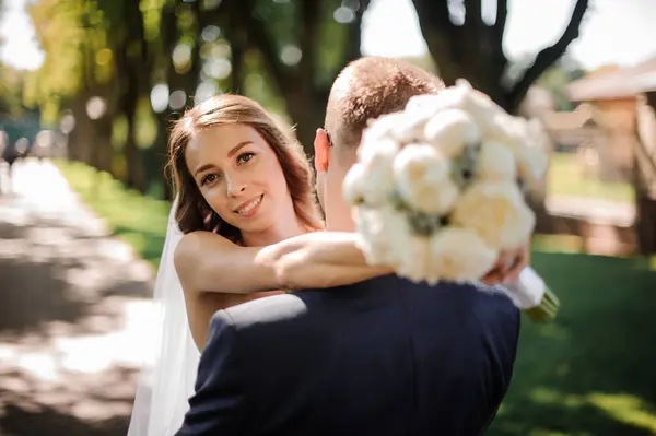 Eleganta brudgummen i en festlig kostym kramar en vacker brud — Stockfoto