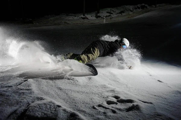 Snowboarder ativo que monta abaixo da inclinação nevada da montanha na noite — Fotografia de Stock