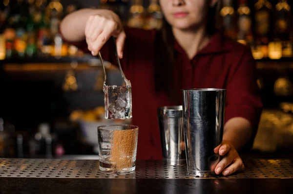 Barmen chica poniendo un gran cubo de hielo en un vaso vacío en un bar — Foto de Stock