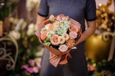 Bej renkli gül ve diğer çiçek bir buket tutan kadın