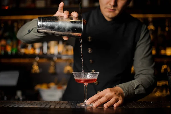 Barman pouring alcoholic drink with campari into the cocktail glass
