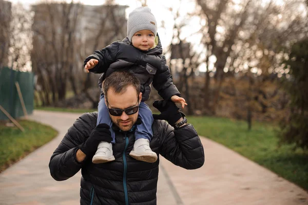 Far i glasögon bär en liten son på hans axlar — Stockfoto