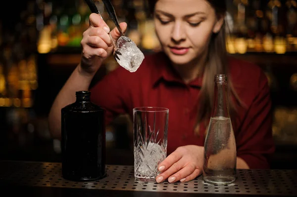 Jovem barman feminina colocando um cubo de gelo em um copo — Fotografia de Stock