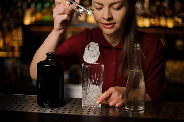 Jovem barman feminino colocando um cubo de gelo em um copo — Fotografia de Stock