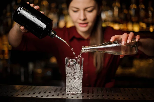 Jonge vrouwelijke barman poting gin en zoete siroop in een glas — Stockfoto