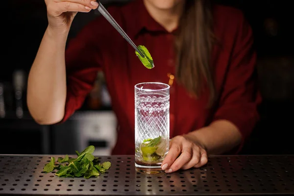 Barkeeperin fügt einem Glas mit Rohrzucker und Limette ein Blatt frische Minze hinzu — Stockfoto