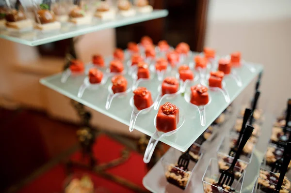 Ensemble de petits apéritifs salés dans un glaçage rouge décoré de tomates séchées au soleil — Photo