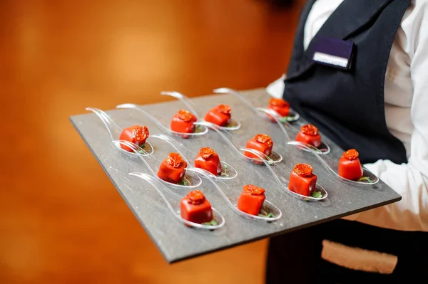Camarero sirviendo un paté de pequeños aperitivos salados en un esmalte rojo decorado con tomate secado al sol y microgreens —  Fotos de Stock