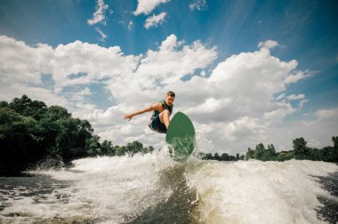 Etkin adam wakesurfing bulutlu gökyüzü ve ağaçlar karşı nehrin gemide
