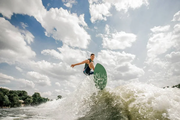 Genç adam eğlenmek wakesurfing gökyüzüne karşı nehrin gemide