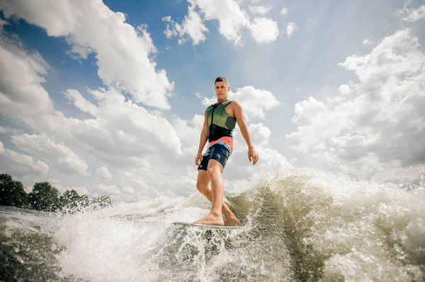 Schöner großer Mann wacht auf dem Brett flussabwärts gegen den wolkenverhangenen Himmel und Bäume — Stockfoto