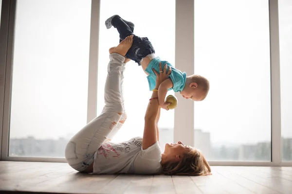 Madre, tendida en el suelo, sosteniendo a su hijito en el aire — Foto de Stock