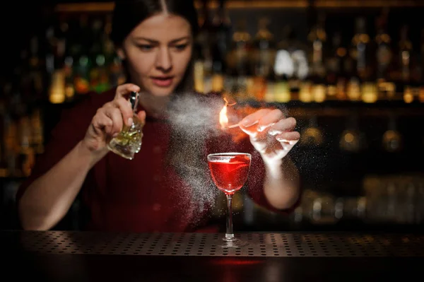 Женщина-бармен брызгает на огонь спичкой над коктейлем — стоковое фото