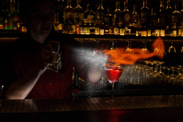 Female bartender spraying on the fire match above the cocktail o