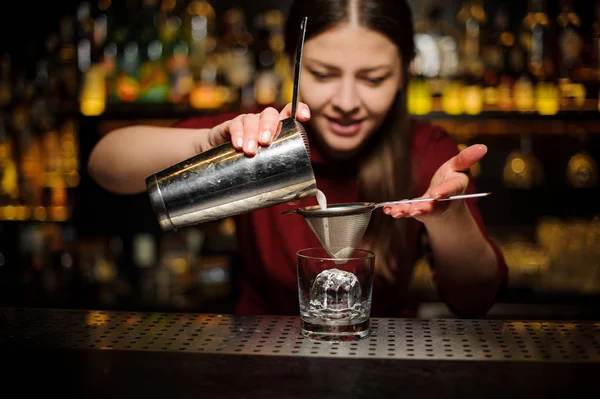 Женщина-бармен наливает коктейль из шейкера через решето — стоковое фото