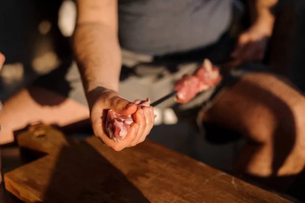 Sitting man stringing pieces of fresh meat on steel skewers — Stock Photo, Image