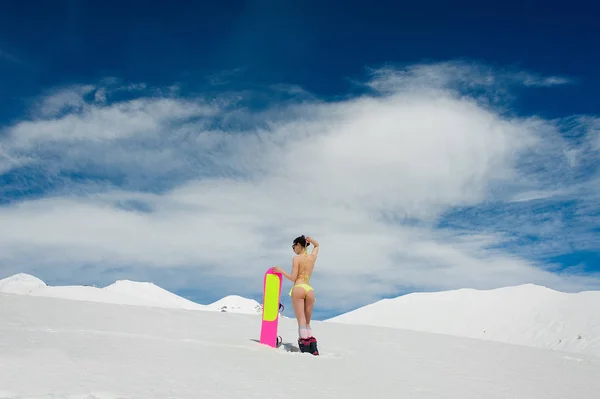 Rückansicht einer heißen Snowboarderin im Badeanzug mit einem rosafarbenen Board auf einem Berg — Stockfoto