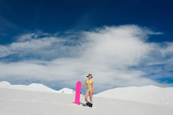 Femme sexy snowboarder en maillot de bain avec une planche rose debout sur un sommet de montagne — Photo