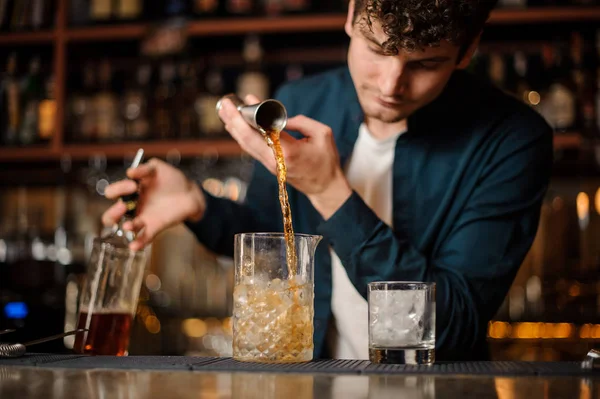 Brunet camarero verter una bebida alcohólica en el vaso con hielo — Foto de Stock