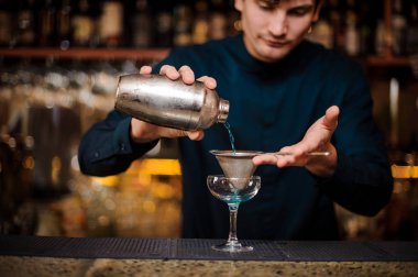 Genç barmen bir süzgeç aracılığıyla bir alkol kokteyl Blue Lagoon filtreler.